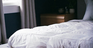  Nachtruhe- Teil eines Bettes mit weißer Bettwäsche. Daneben steht ein brauner Nachtisch.