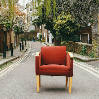 zurückgelassener roter Sessel nach einer Zwangsräumung steht auf der Straße. Dahinter befinden sich Laternen, Bäume und Häuser