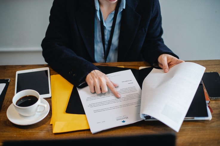 Eine Person sitzt an einem Schreibtisch und zeigt mit ihrem Finger auf einen Vertrag.