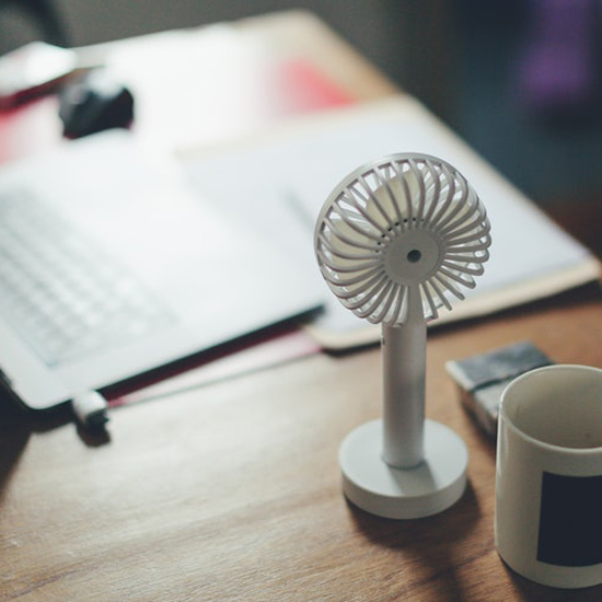  weißer Ventilator steht neben einer weißen Tasse auf einem Holztisch für eine kühle Wohnung.