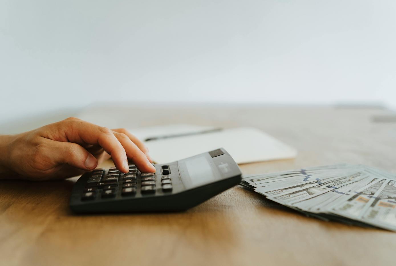 Hand tippt etwas in Taschenrechner ein, der auf dem Tisch liegt.